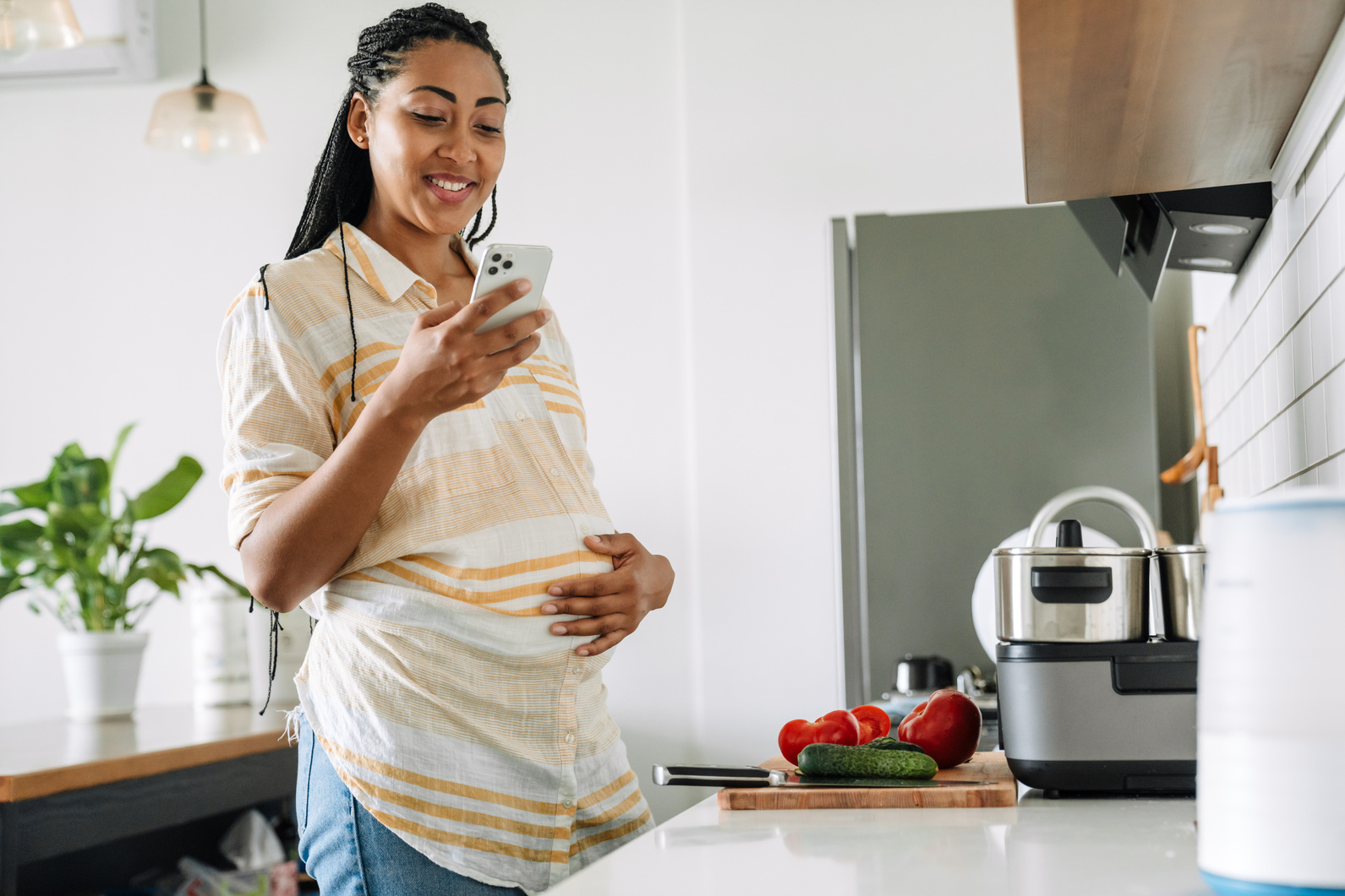 Black Pregnant Woman Smiling and Using Mobile Phone in Kitchen
