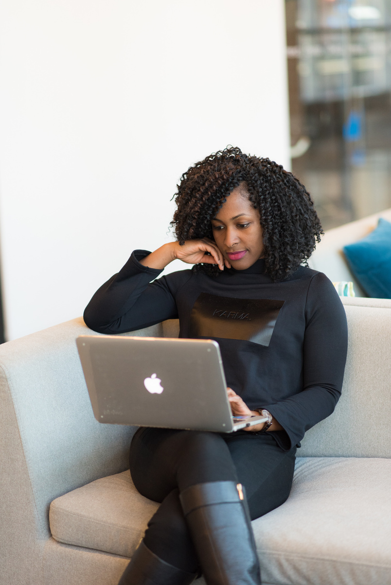 Woman in black outfit with MacBook sitting on a couch.